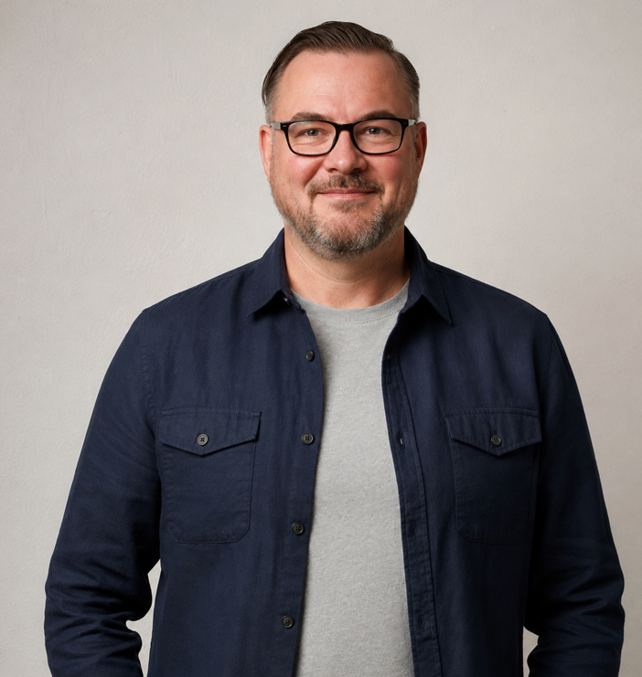 Rob Budd Smiling man with glasses wearing a navy shirt over a grey t-shirt.